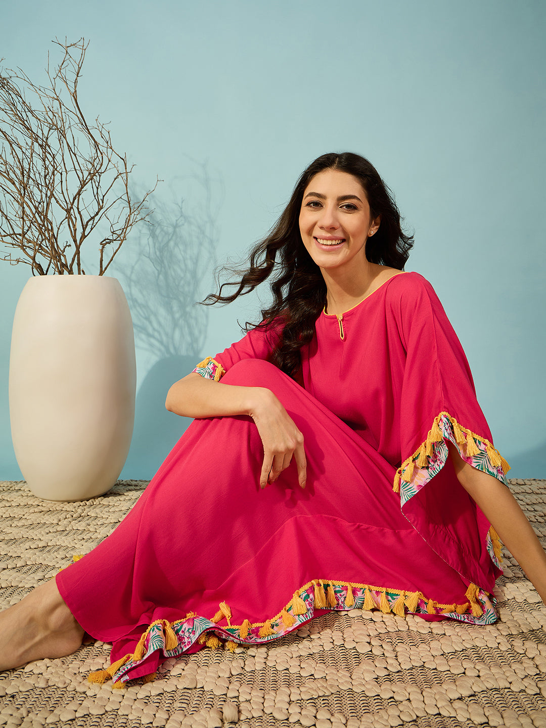 Elegant pink kaftan for lounging, with yellow tassel accents and a slim fit.
