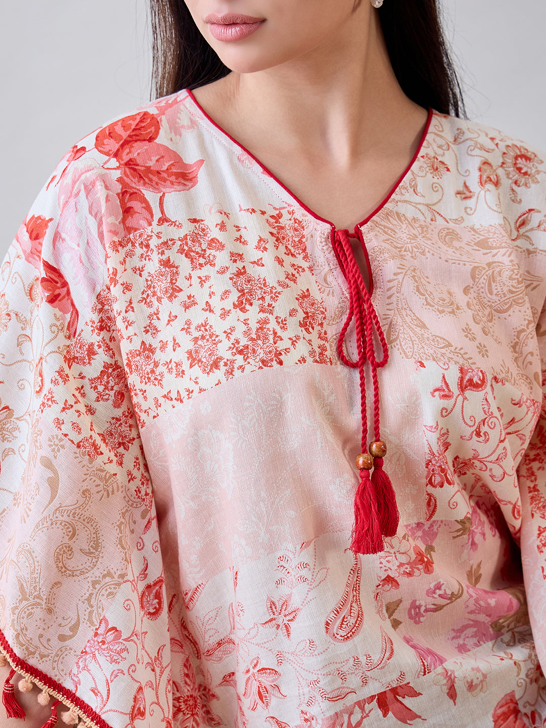 Stylish beige cotton kaftan top with red pom-poms and lace details, combining elegance with a fun, boho flair.

