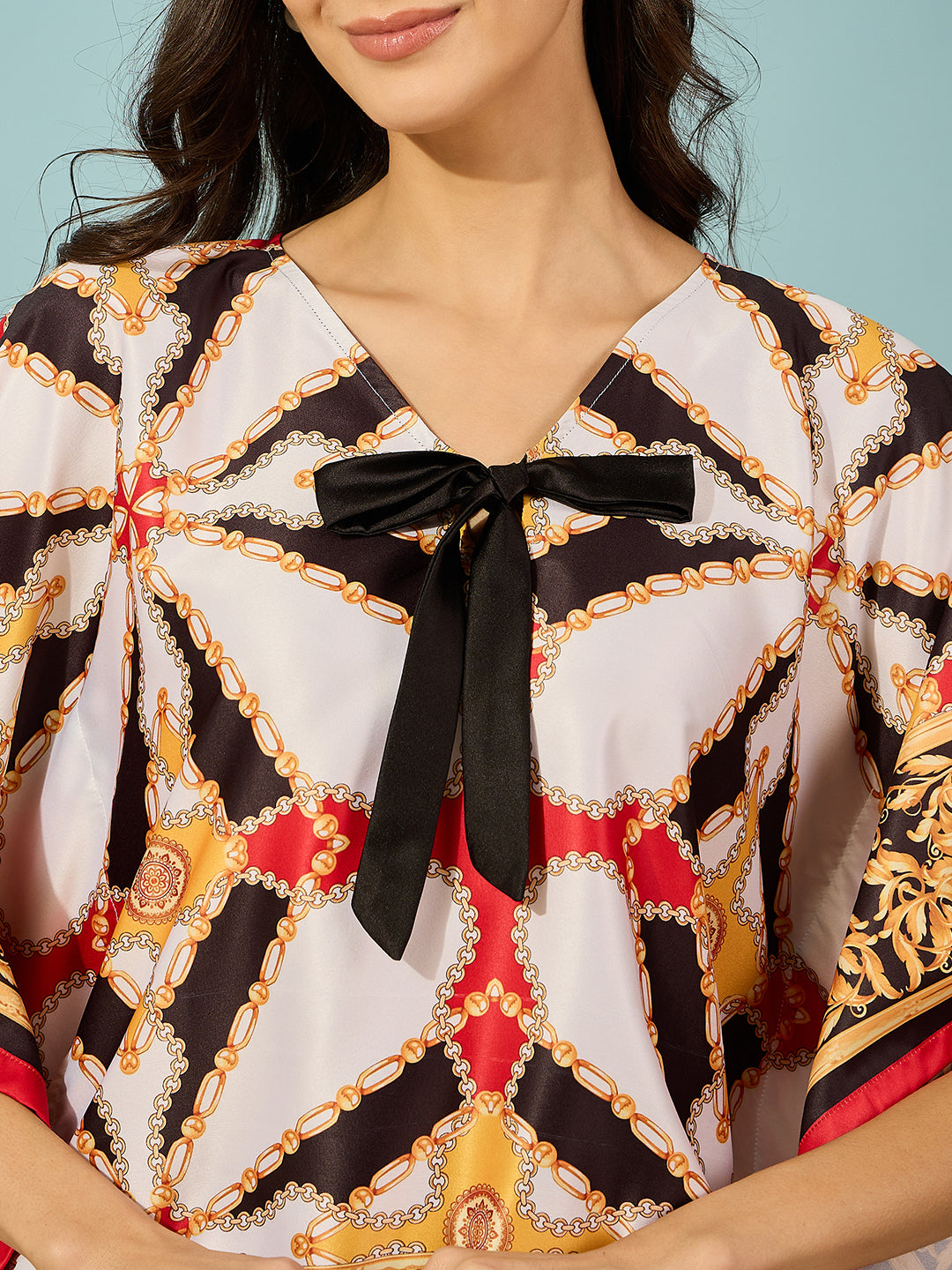 Turn heads with a black satin kaftan top in Baroque print, accented with a playful bow detail.
