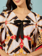 Turn heads with a black satin kaftan top in Baroque print, accented with a playful bow detail.
